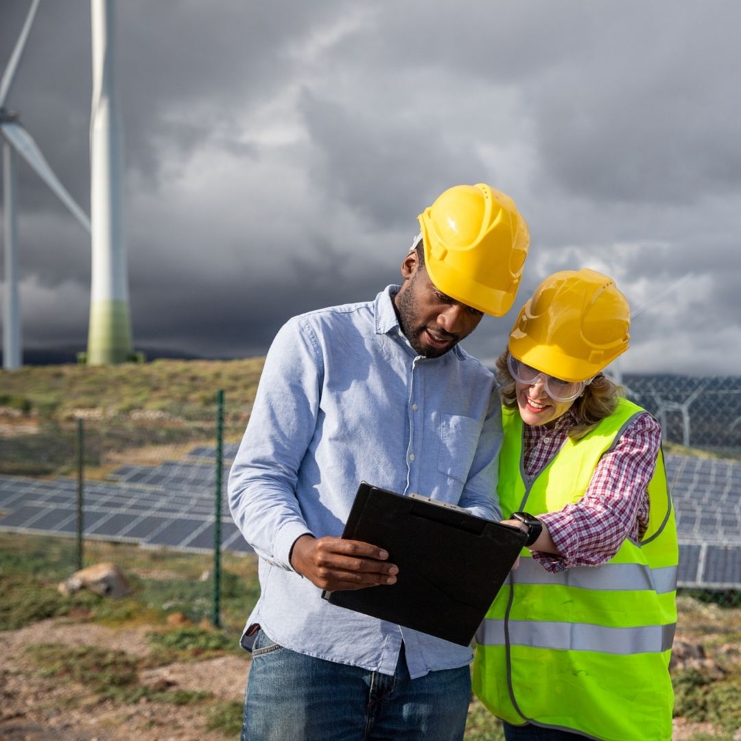 Engineers in safety gear reviewing plans at a renewable energy site — recruitment for the energy and infrastructure sector