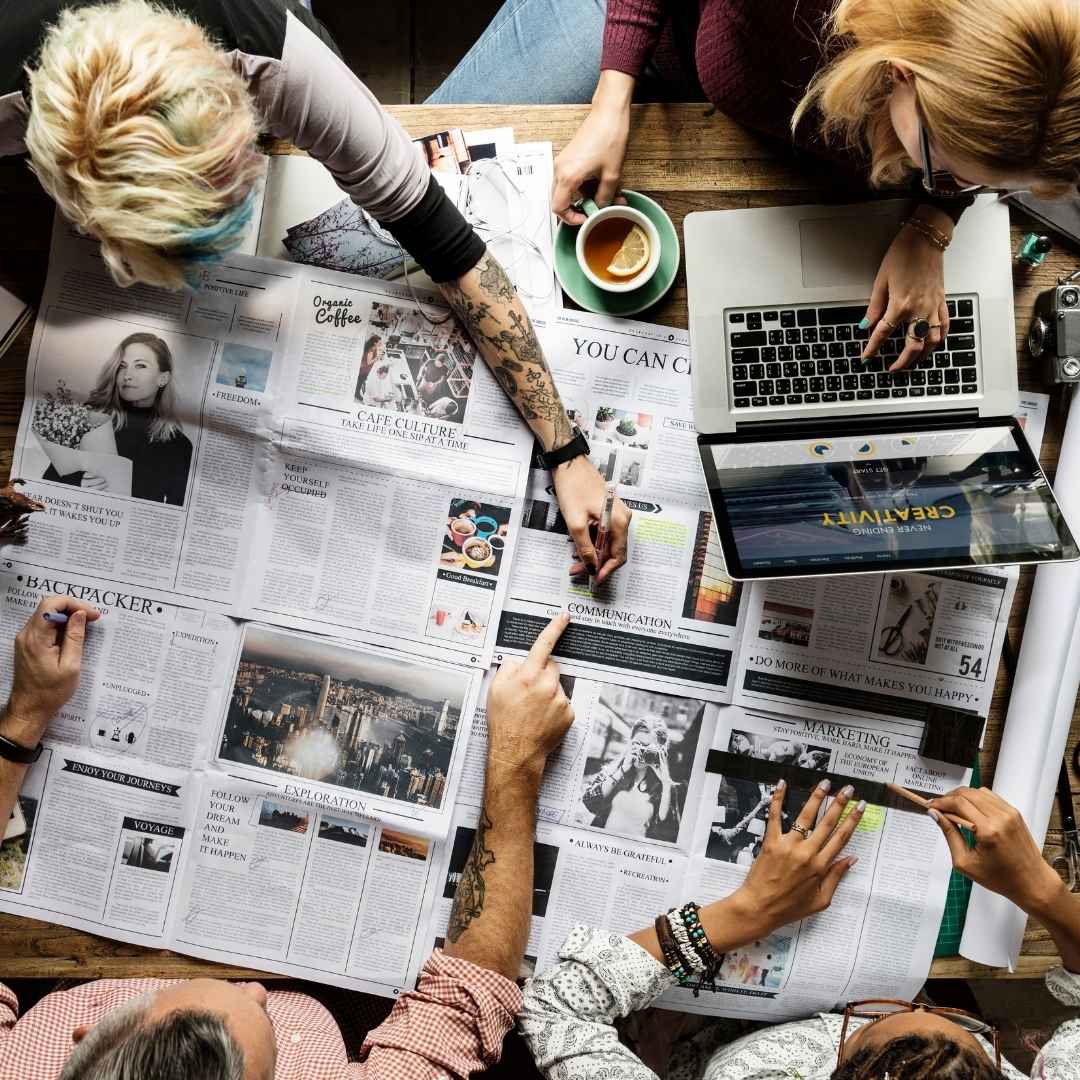 Creative team brainstorming with print media and laptops — media and advertising recruitment services.