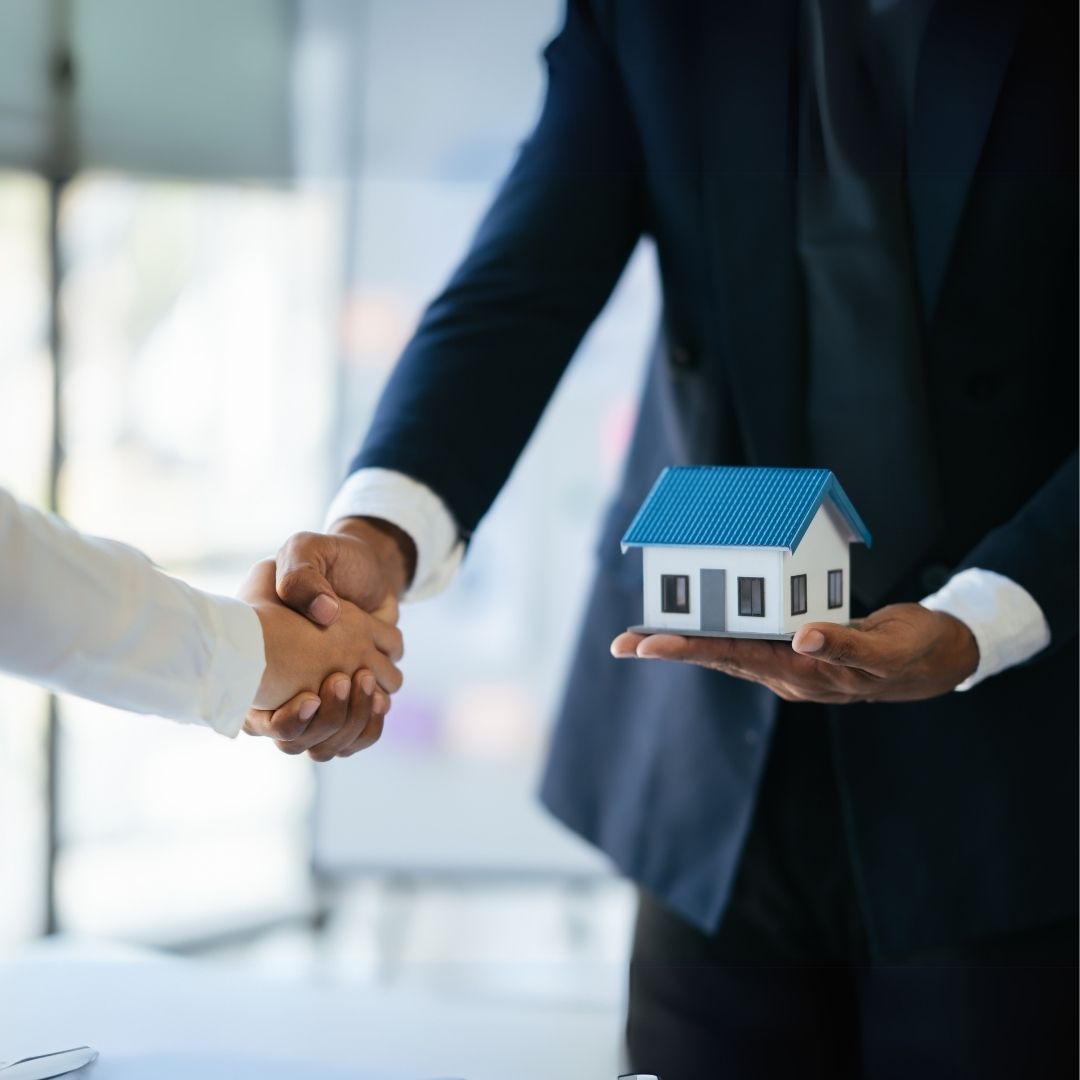 Business professionals shaking hands over a miniature house model — real estate staffing services.